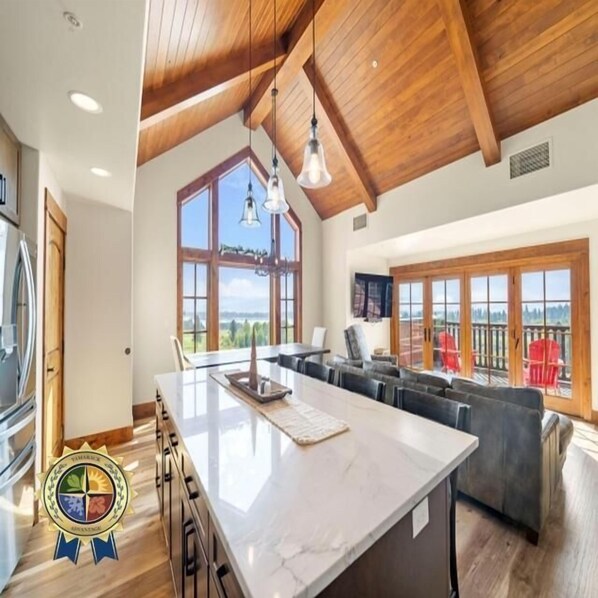 A spacious kitchen with a large island, wooden ceiling beams, and large windows offering a view of the outdoors.