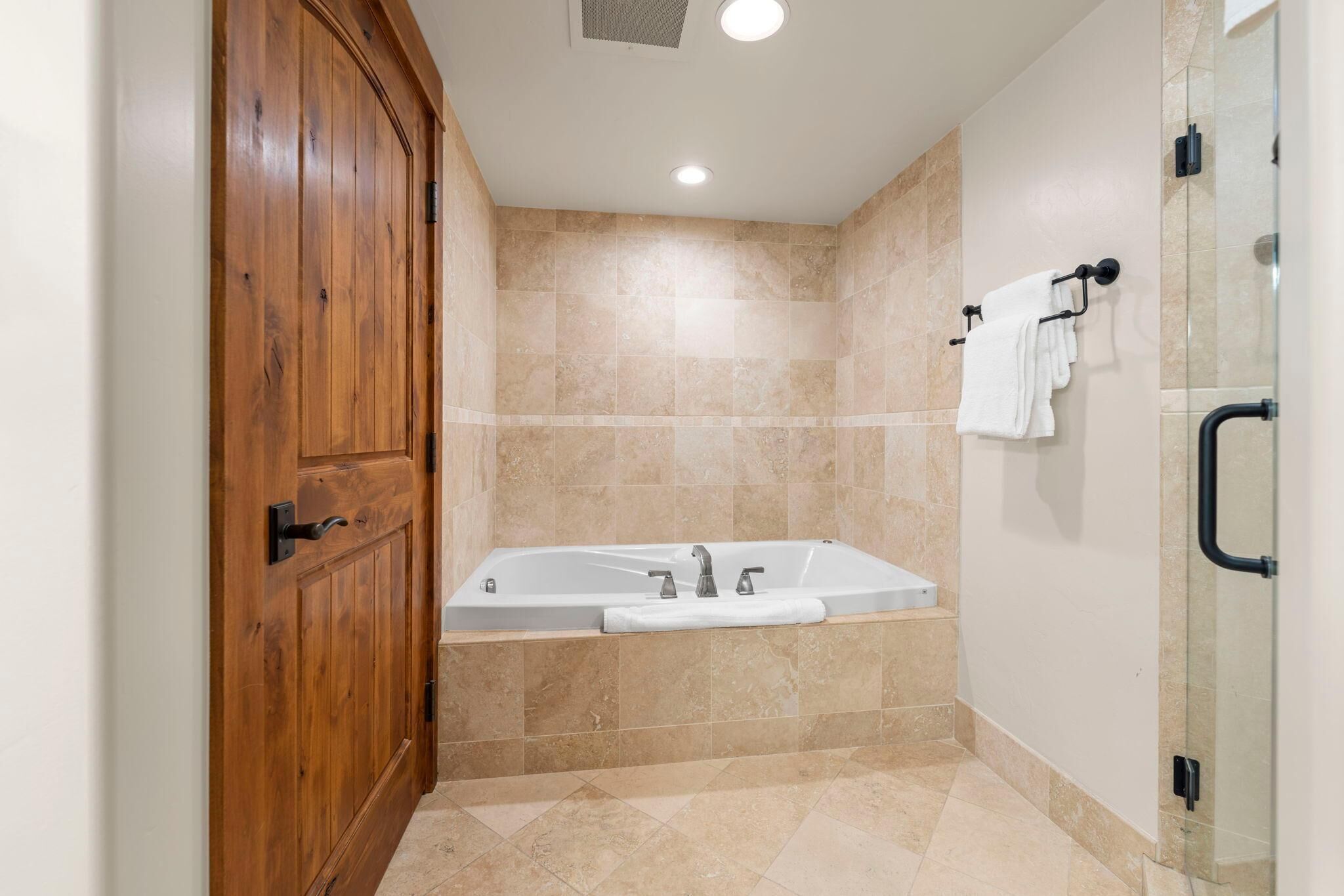 Une salle de bain avec une porte en bois, une baignoire et une cabine de douche en verre.