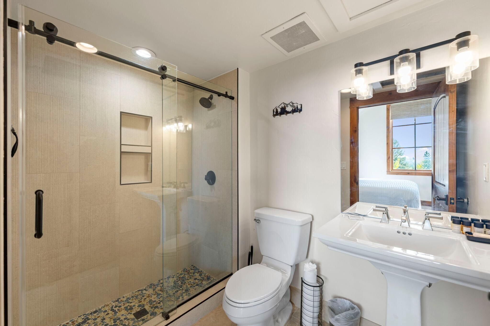 A modern bathroom with a glass-enclosed shower, a white toilet, and a sink with a large mirror above it.