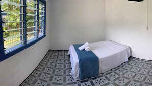 Een kleine kamer met een enkel bed, een raam, een deur en vloertegels met een patroon.