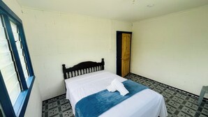 Een enkel bed in een kamer met een kamer met een patroon vloer, een raam met blauwe rand, en een deur.