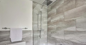 Une salle de bain moderne avec une douche à parois de verre, des carreaux de marbre et une serviette blanche posée sur un radiateur.