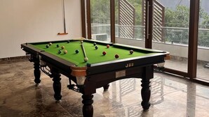 Een pooltafel in een kamer met grote ramen en uitzicht op een gebouw.