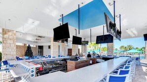 A modern outdoor bar area with a long counter, blue chairs, and a Christmas tree. - Luxury 7BR Villa w/Pool & Resort Access, Sleeps 16 – 10 Min to Disney (Davenport)
