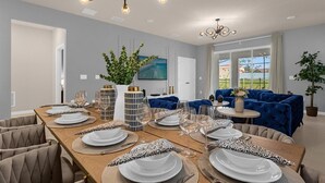 A dining area with a long table set for six, surrounded by blue sofas and a round coffee table. - Luxury 7BR Villa w/Pool & Resort Access, Sleeps 16 – 10 Min to Disney (Davenport)