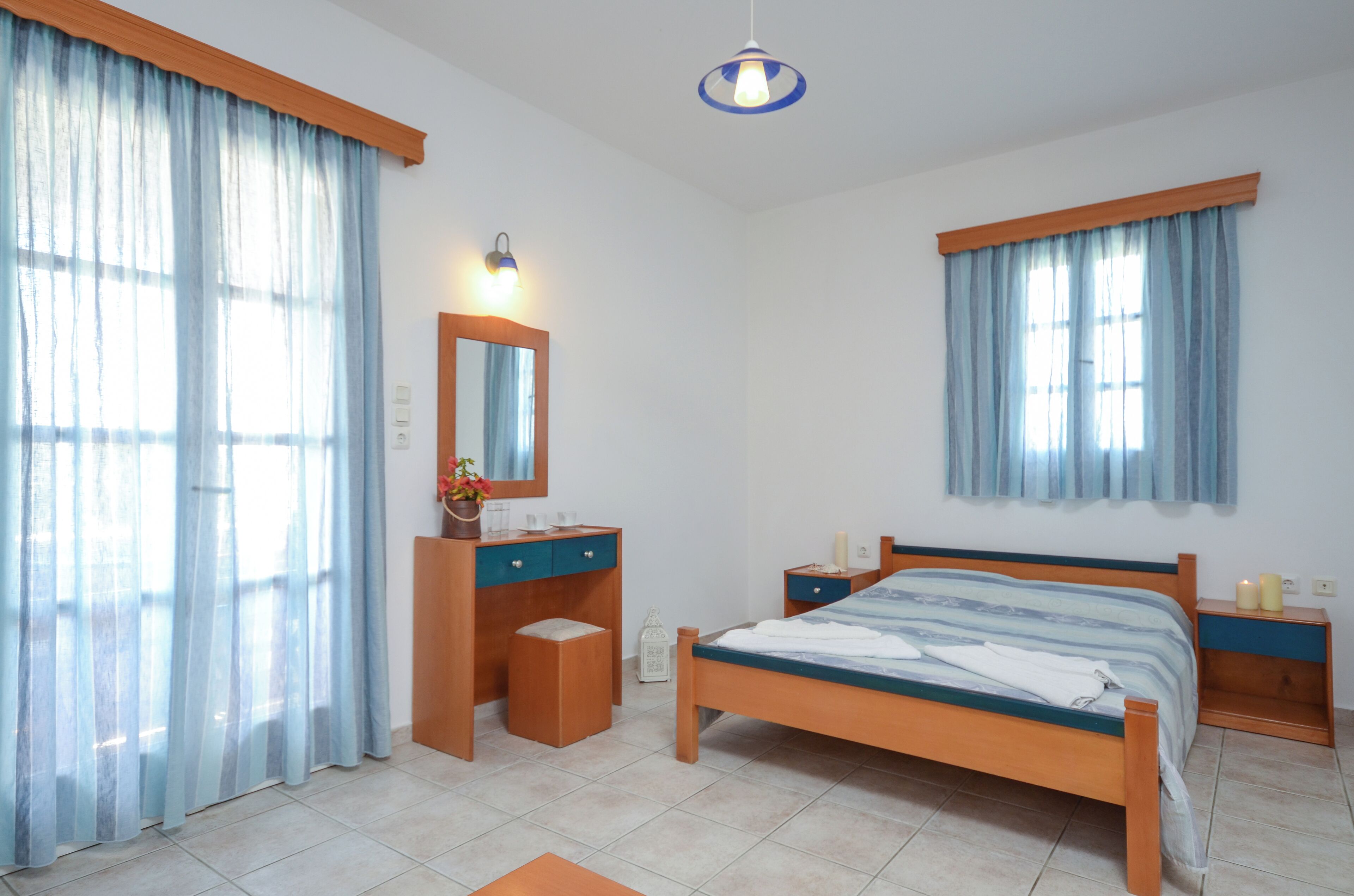 A bedroom with a bed, a wooden dresser, a nightstand, a mirror, and a window with curtains.