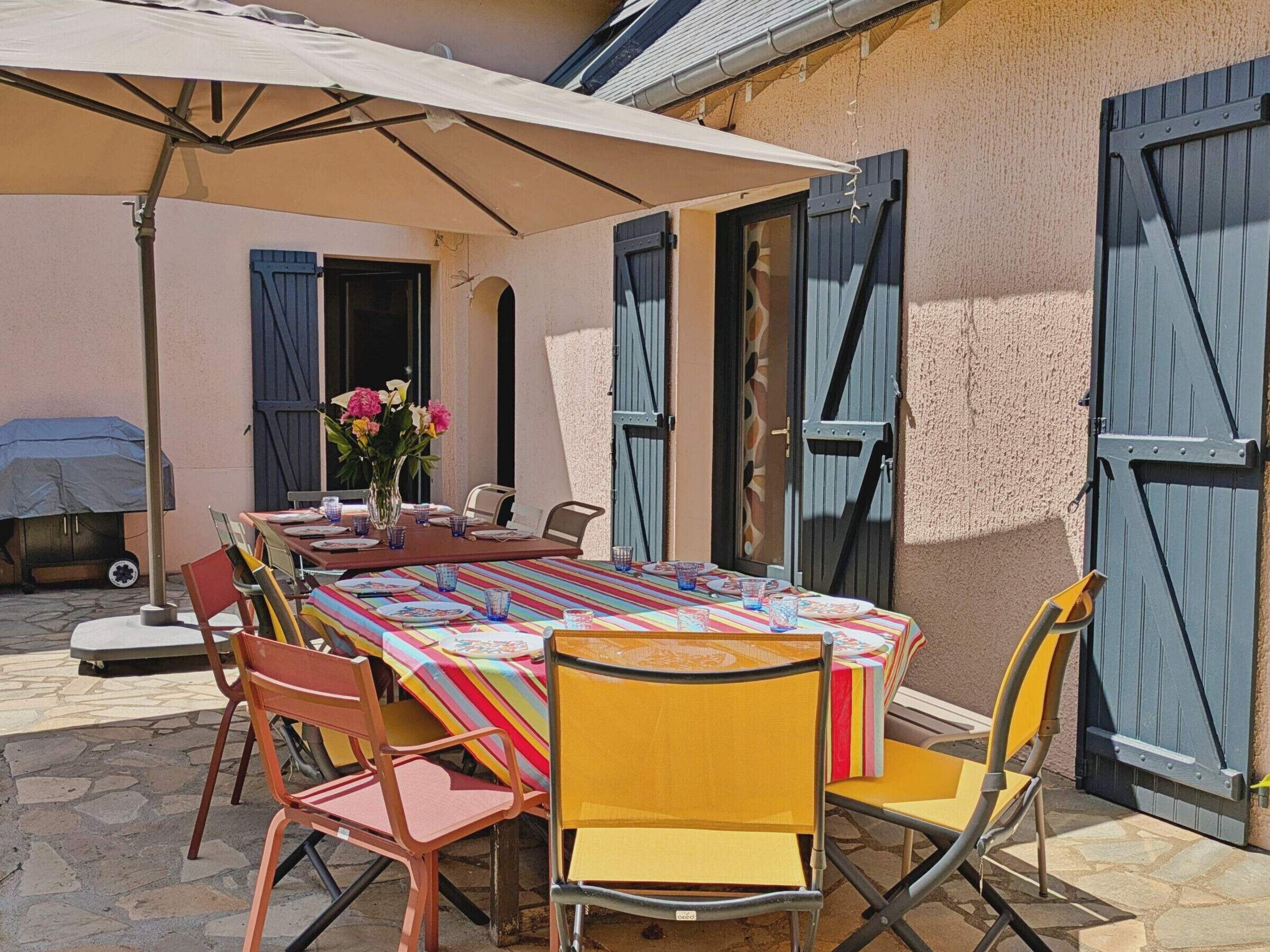 Een buiten eethoek met een tafel voor vier personen, omringd door stoelen, onder een grote parasol.