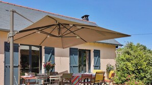 Eine Terrasse mit Tisch und Stühlen, einem großen Sonnenschirm und einem Haus mit geneigtem Dach.