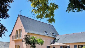 Ein zweistöckiges Haus mit geneigtem Dach, einem Balkon und einem kleinen Gartenbereich mit Sitzgelegenheiten.