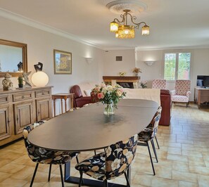 Een ruime eethoek met een grote ronde tafel, een bloemstuk en moderne stoelen.
