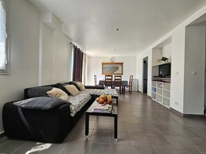 Una sala moderna con un sofá, una mesa de centro con revistas, un comedor con mesa y sillas, y un televisor en un estante.