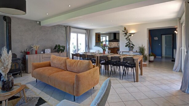A spacious living area with a sofa, dining table, and chairs. A kitchen is visible in the background. - Spacious cottage for 12 with private garden and spa in Chevrières (Chevrières - Loire)