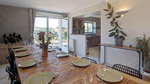 A dining area with a table set for six, a kitchen in the background, and a view of the countryside. - Spacious cottage for 12 with private garden and spa in Chevrières (Chevrières - Loire)