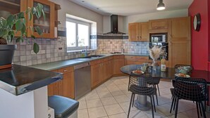 A modern kitchen with wooden cabinets, a black countertop, a dining area with a round table and chairs, and a red accent wall. - Spacious cottage for 12 with private garden and spa in Chevrières (Chevrières - Loire)