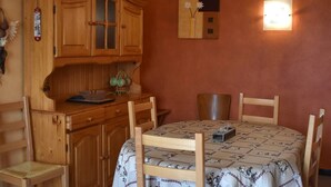 A small dining area with a wooden table and chairs, a cabinet with glass doors, and a wall-mounted light fixture. - Bright 3-room apartment - Pyrenees view and parking (Font-Romeu-Odeillo-Via)