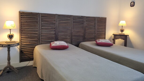 A room with two beds, each with a pillow and a lamp. There is a wooden headboard behind the beds, and a small table with a lamp on the left side.
