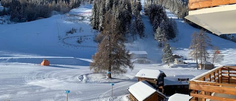 A snow-covered ski resort with wooden cabins, a ski lift, and a mountain backdrop.