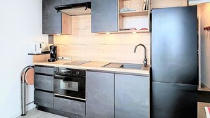 A modern kitchen with a built-in oven, a sink, and a black refrigerator. - Ski-in/Ski-out Apartment with Twin Balconies and Free WIFI (Le Corbier)