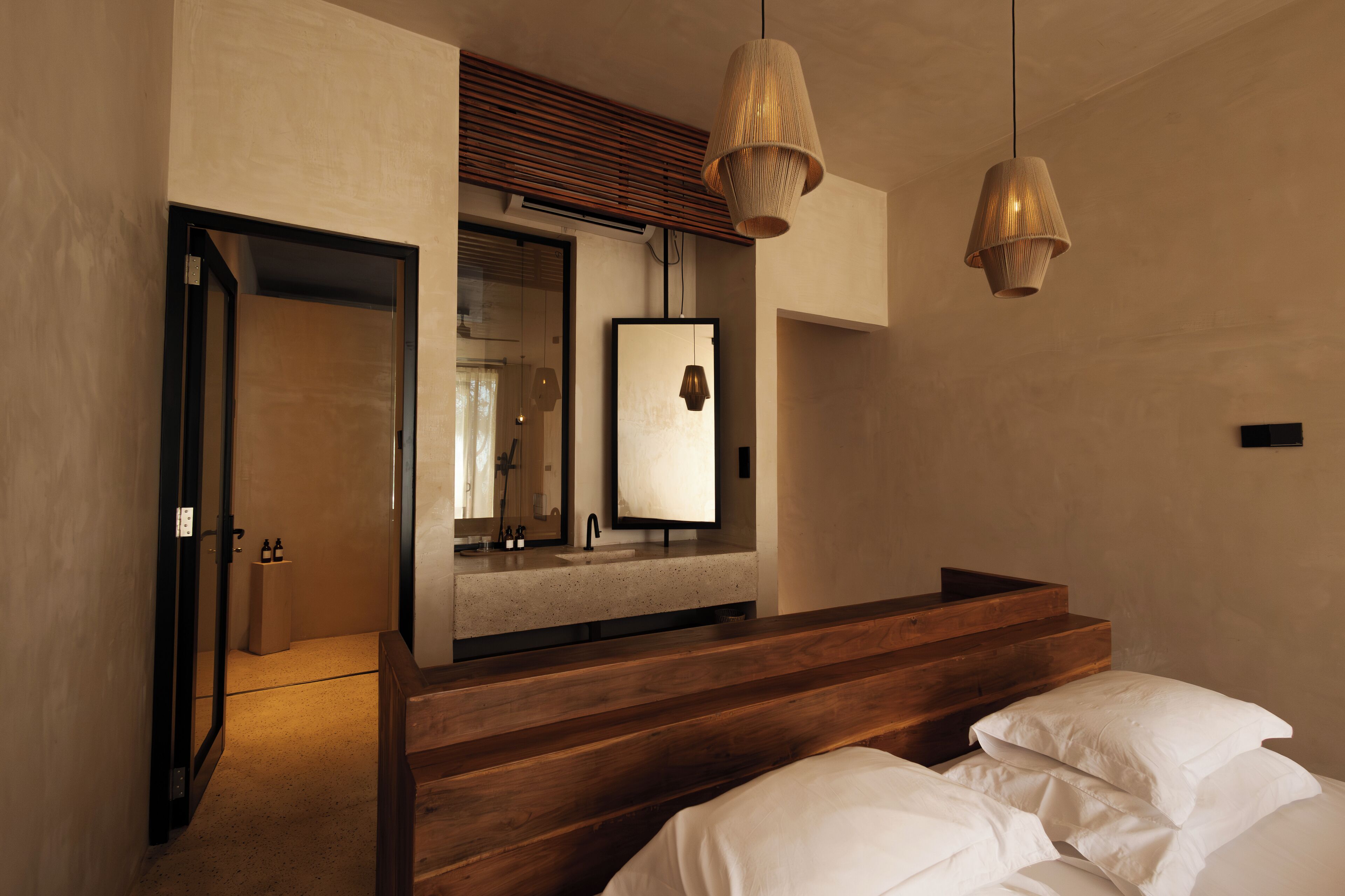 A modern bedroom with a wooden headboard, a large mirror, and two hanging light fixtures.