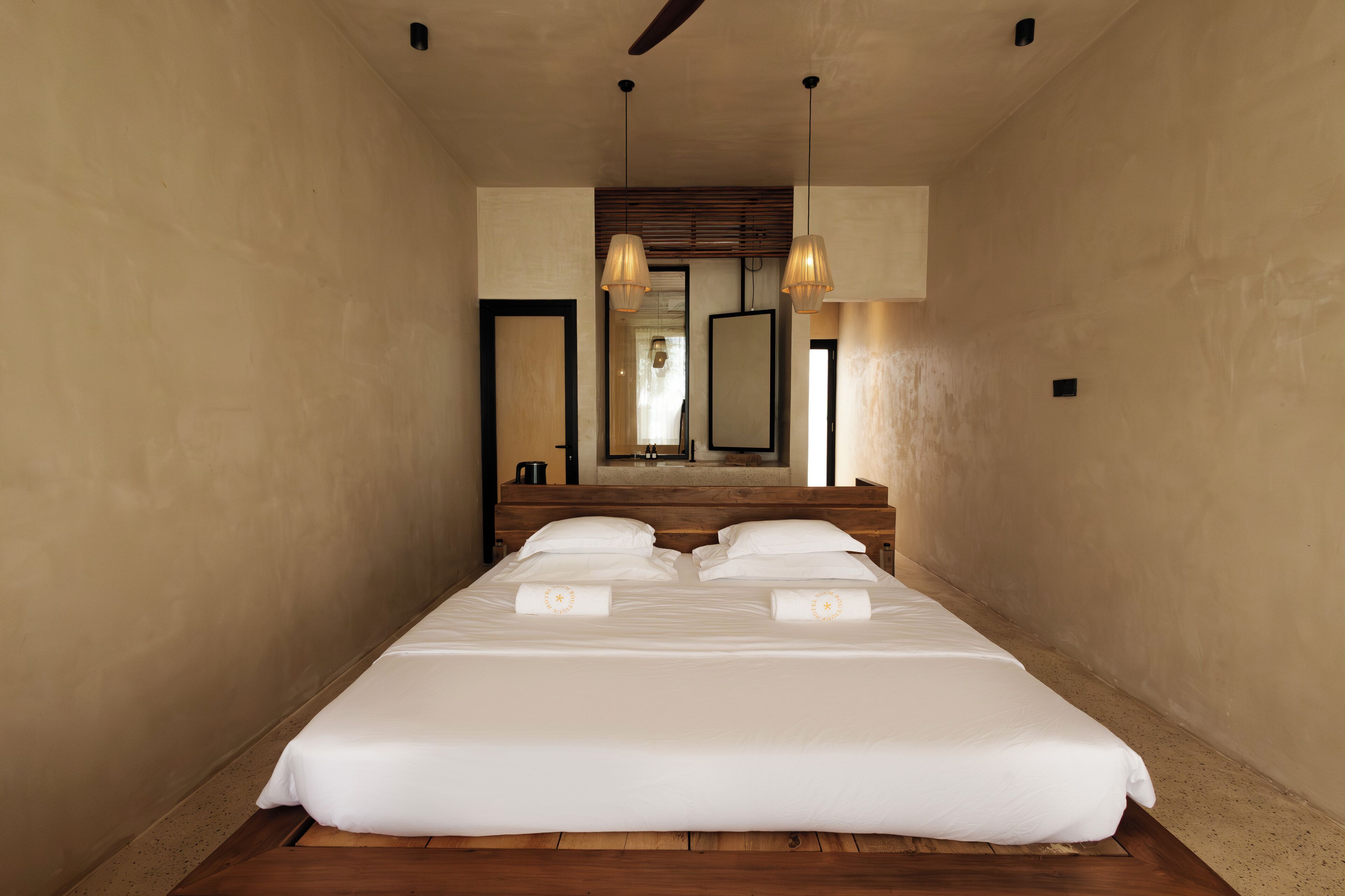Una cama grande y bien hecha con sábanas blancas y dos almohadas, cabecera de madera y dos lámparas colgantes.