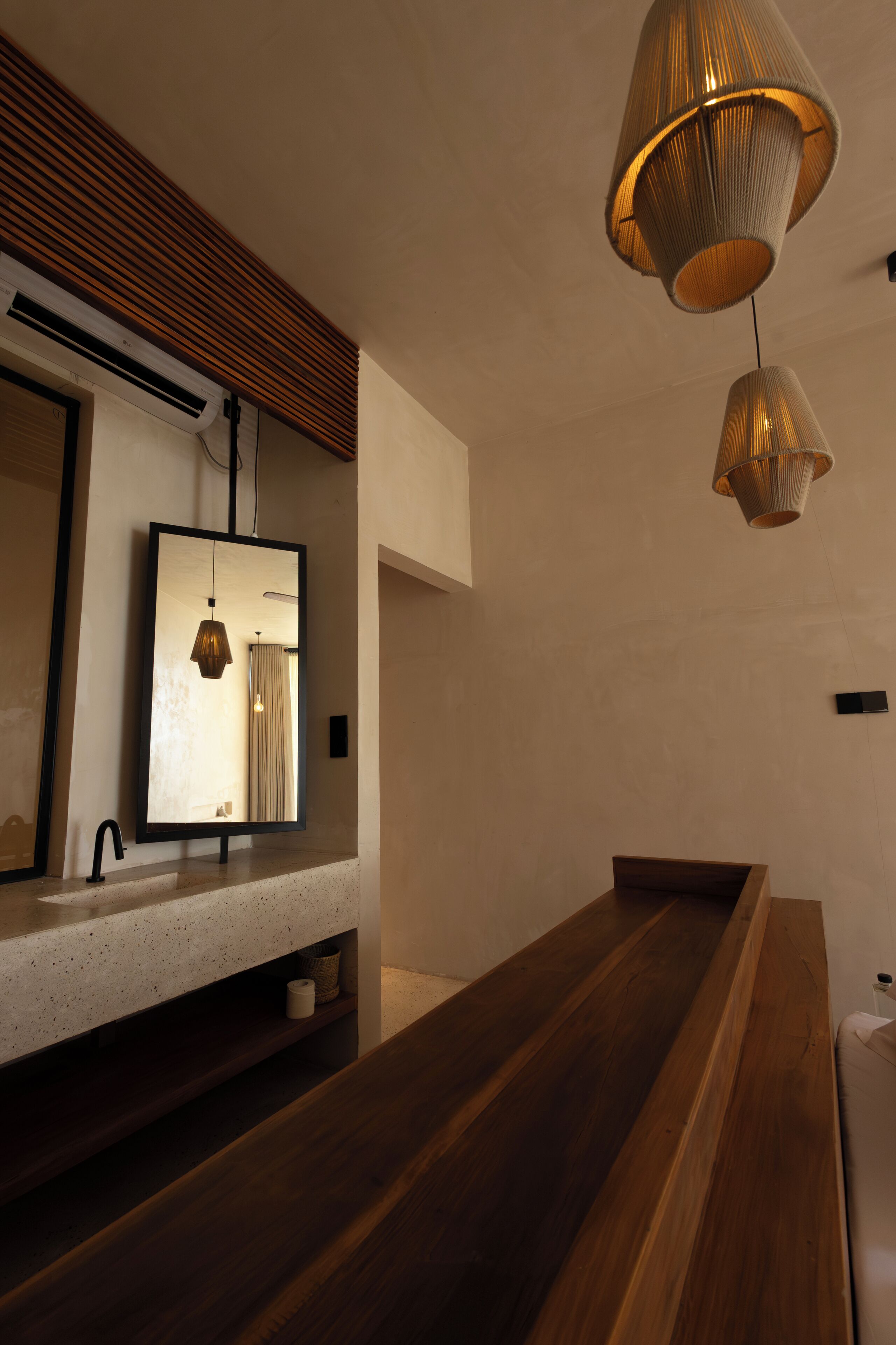 A modern bathroom with a wooden bench, a large mirror, and pendant lighting.