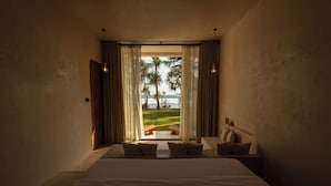 A bedroom with a large bed, a view of the ocean, and a patio area with a table and chairs. - Neem Boutique Hotel (Kamburugamuwa)