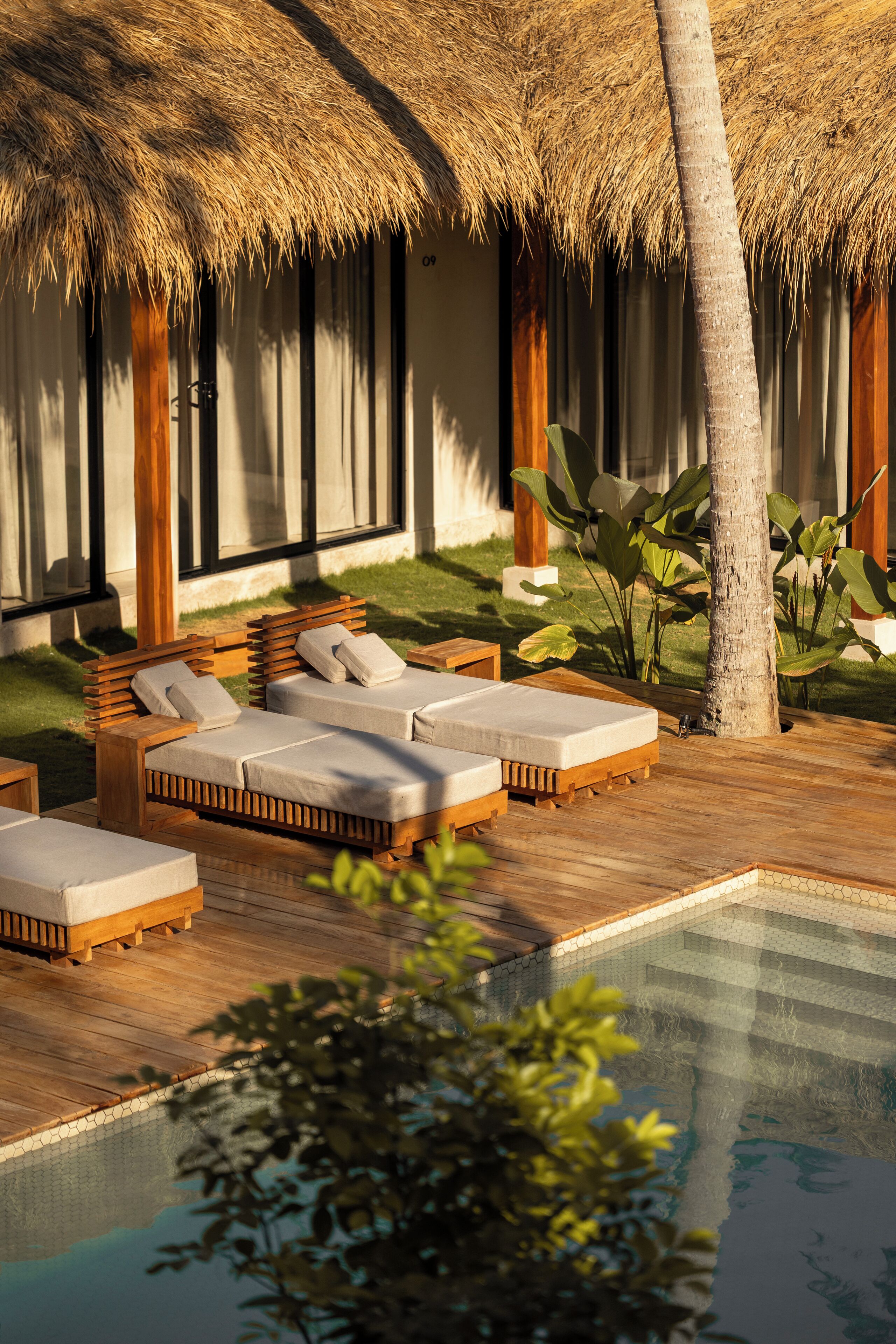 A poolside area with wooden lounge chairs and a thatched roof structure.