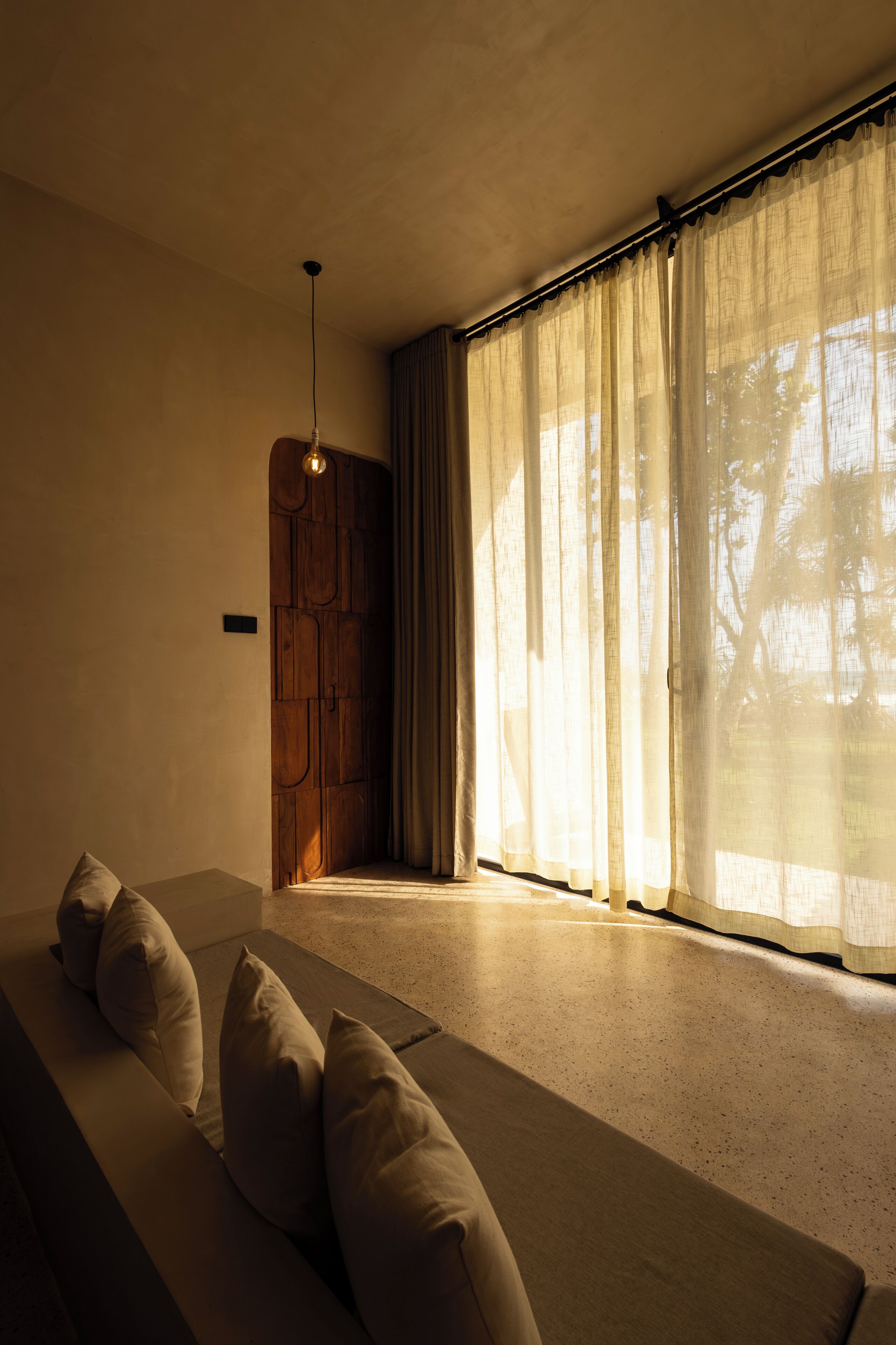 A room with a sofa, a wooden door, and sheer curtains.