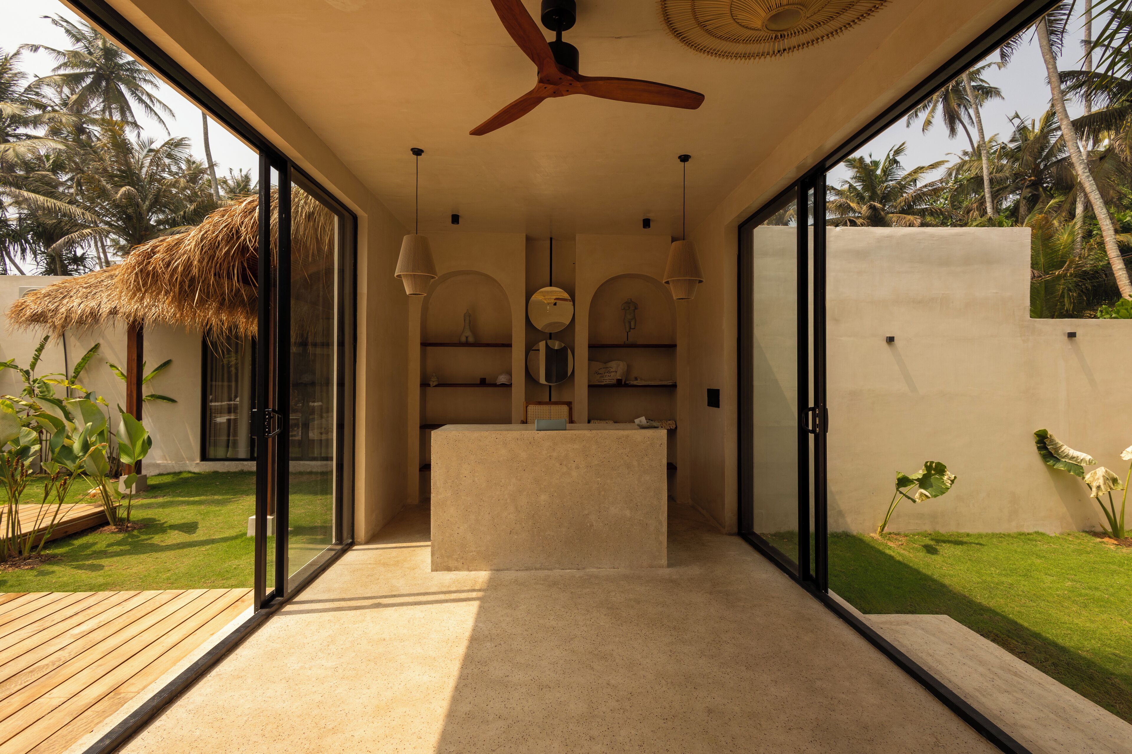 A modern interior with a central reception desk, glass doors leading to a garden, and a ceiling fan.