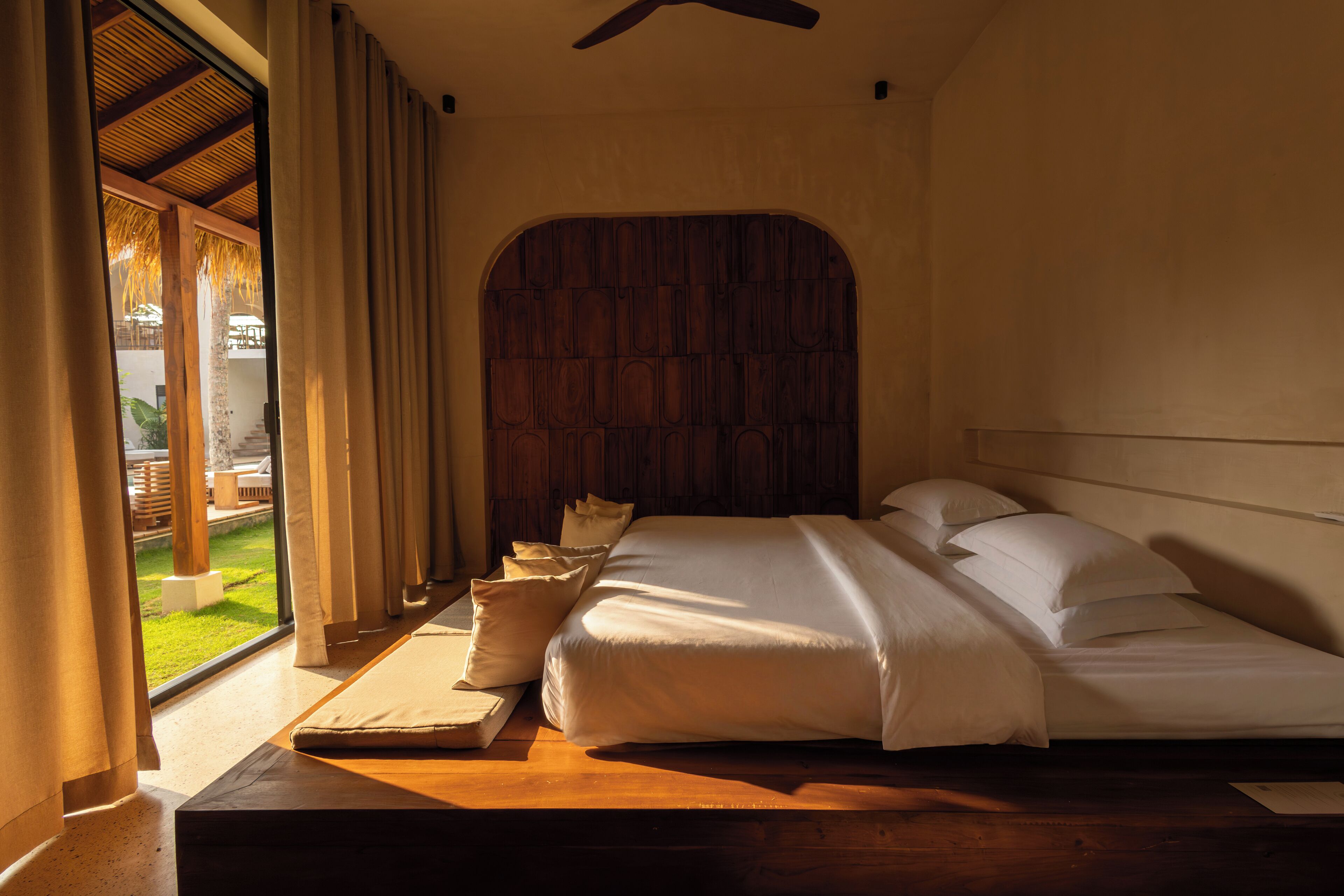 Une chambre avec un grand lit, une tête de lit en bois et une vue sur l’extérieur.