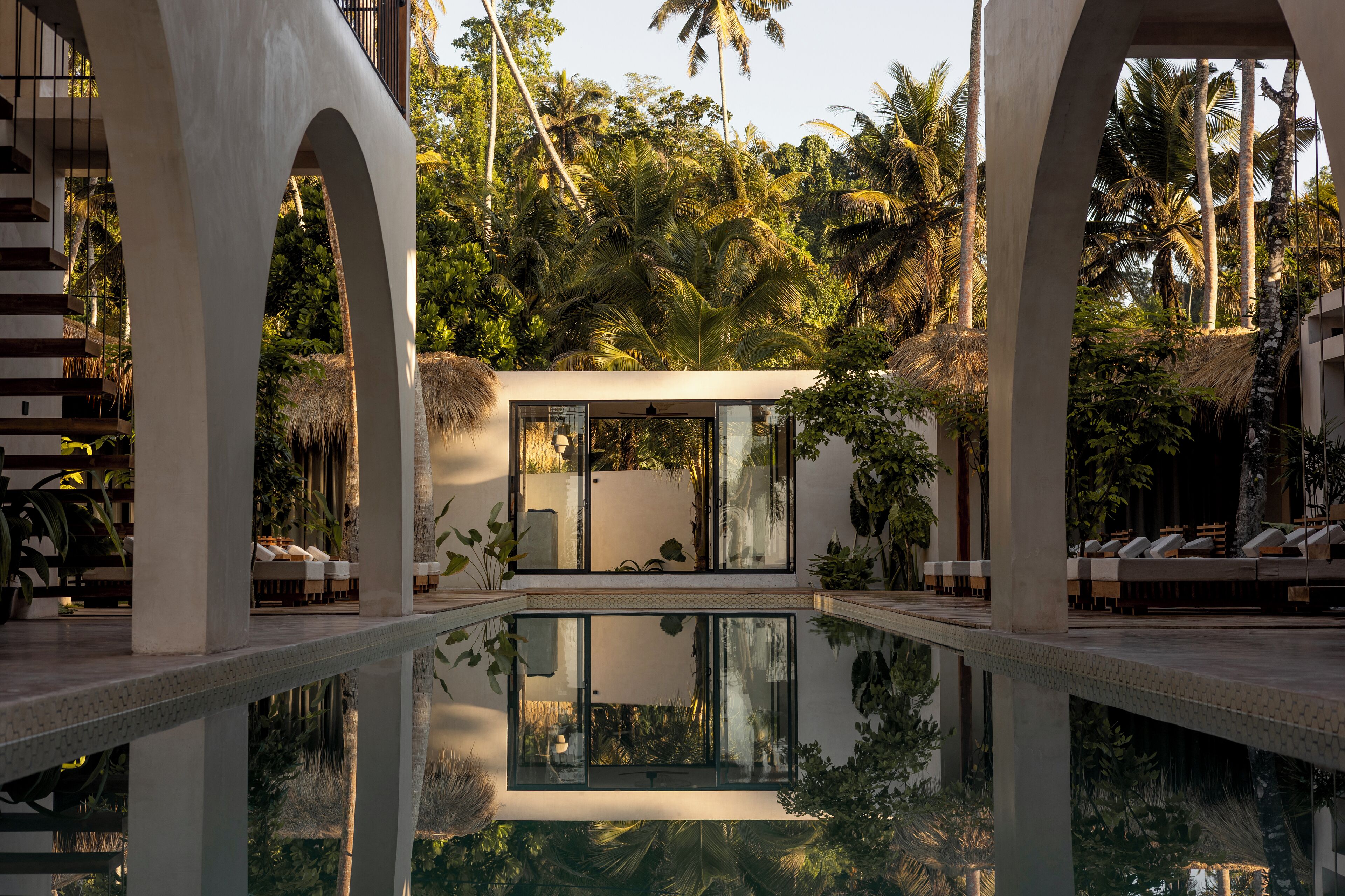 A modern pool area with clear water, surrounded by palm trees and architectural arches.