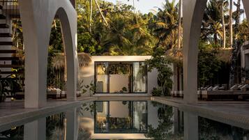 A modern pool area with clear water, surrounded by palm trees and architectural arches.