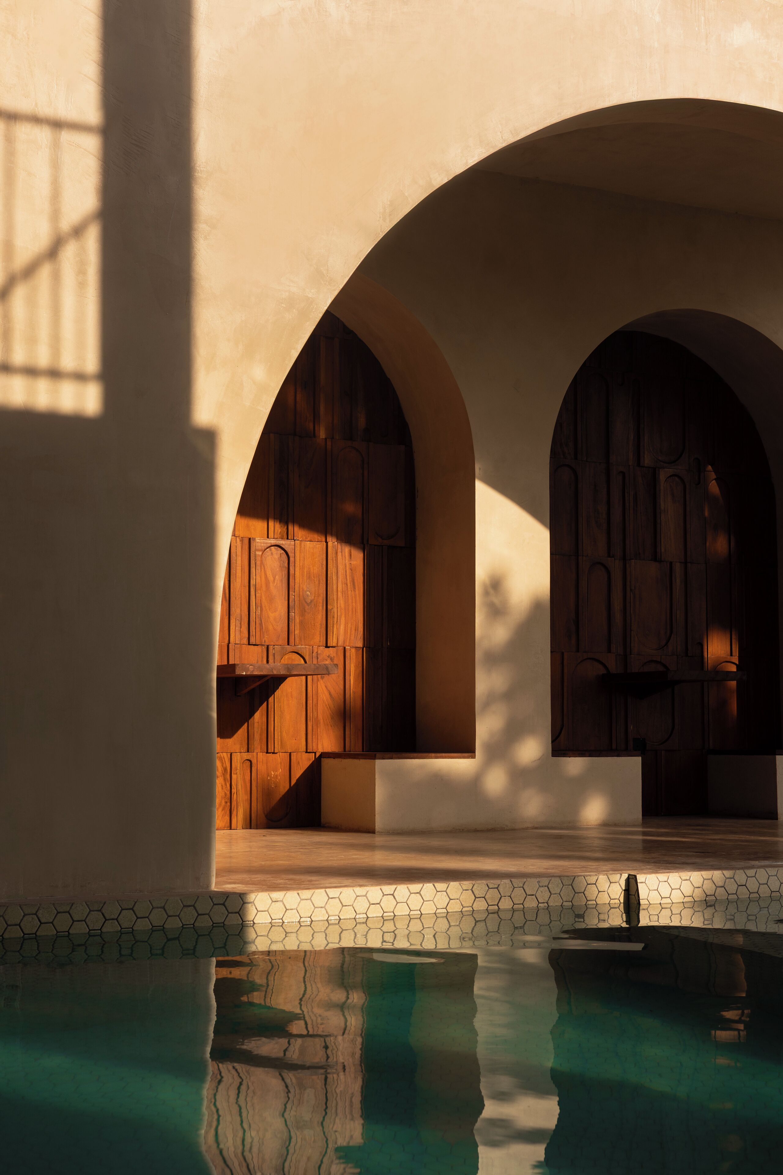 Zona de piscina con puertas de madera arqueadas y borde de piscina con mosaicos.
