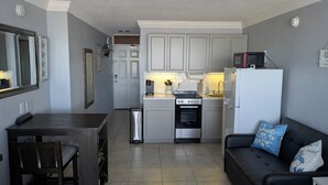 A compact kitchen with white cabinets, a stove, a microwave, and a refrigerator. There's a dining table with chairs and a black sofa with decorative pillows. - Beachfront Suite in Daytona Beach, FL with direct full ocean view!  5th Floor (Daytona Beach)