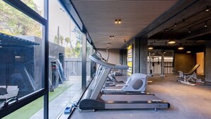 A gym with treadmills, weight machines, and a large window overlooking a brick building.