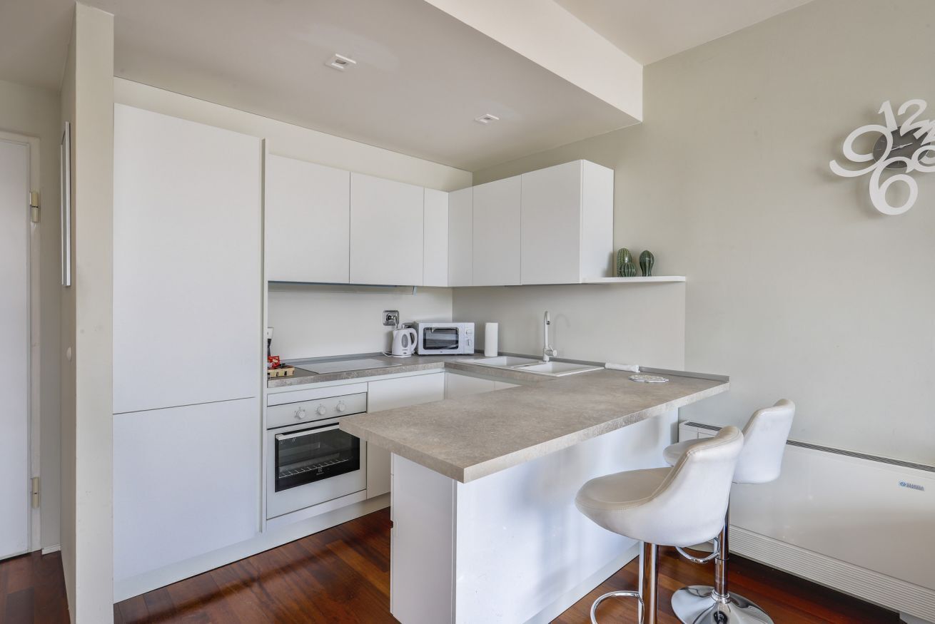 Una cocina moderna con armarios blancos, una isla central con taburetes de bar, microondas y horno empotrado.