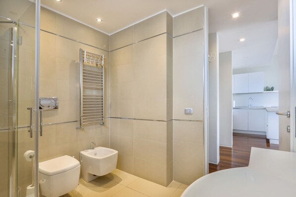 A modern bathroom with a glass shower enclosure, a toilet, a bidet, and a sink.