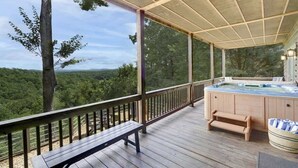 A wooden deck with a hot tub, a bench, and a view of a forested landscape. - Luxury Cabin with Hot Tub & Lake Views (Blue Ridge)