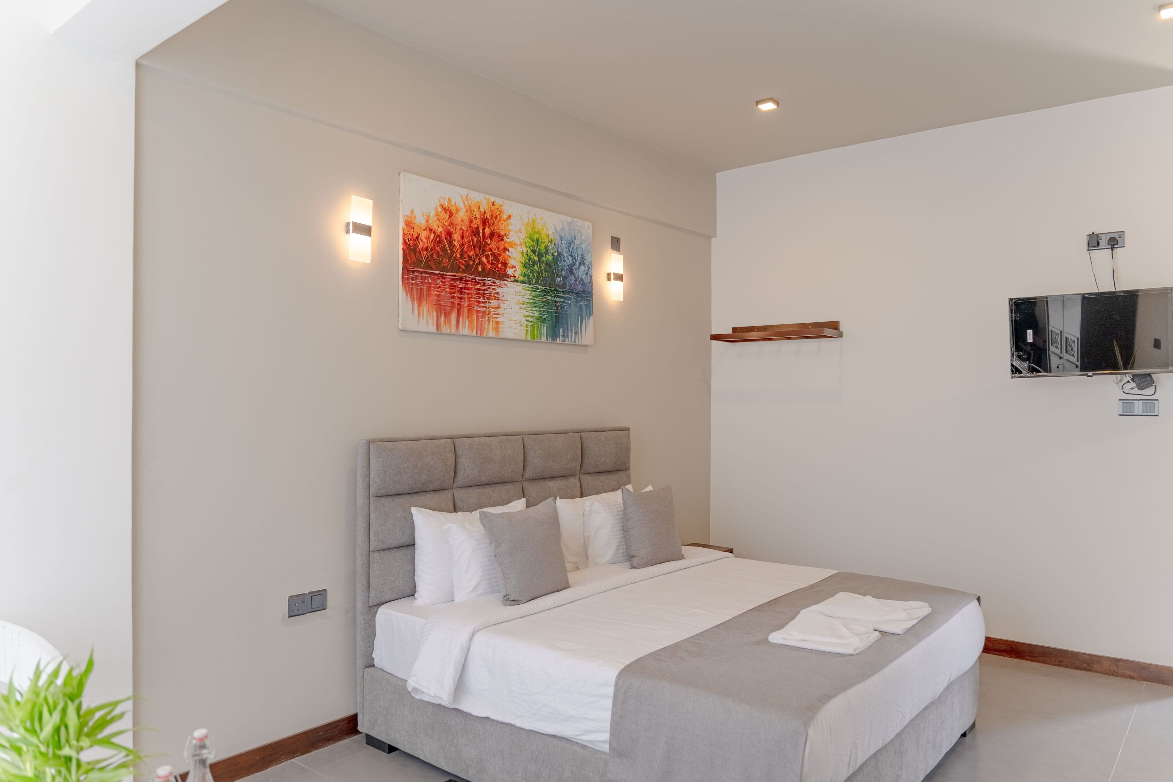 Ein modernes Schlafzimmer mit einem großen Bett, einer Kopfteil, einem an der Wand montierten Fernseher und einem Gemälde.