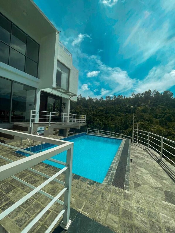 Un edificio moderno con piscina, rodeado por una terraza de piedra y una barandilla de metal.