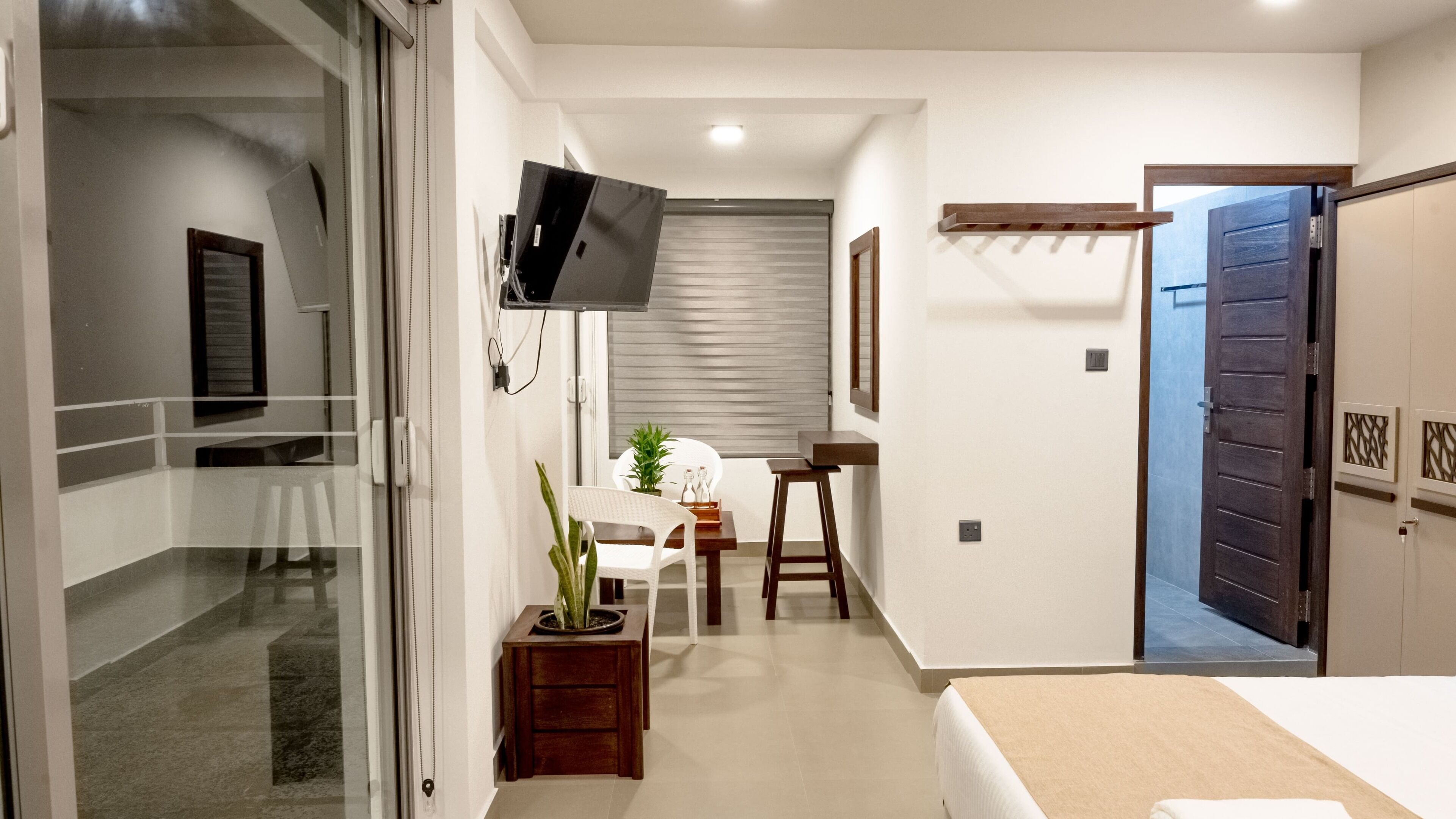 A hotel room with a bed, a TV mounted on the wall, a small table with a plant, and a chair.