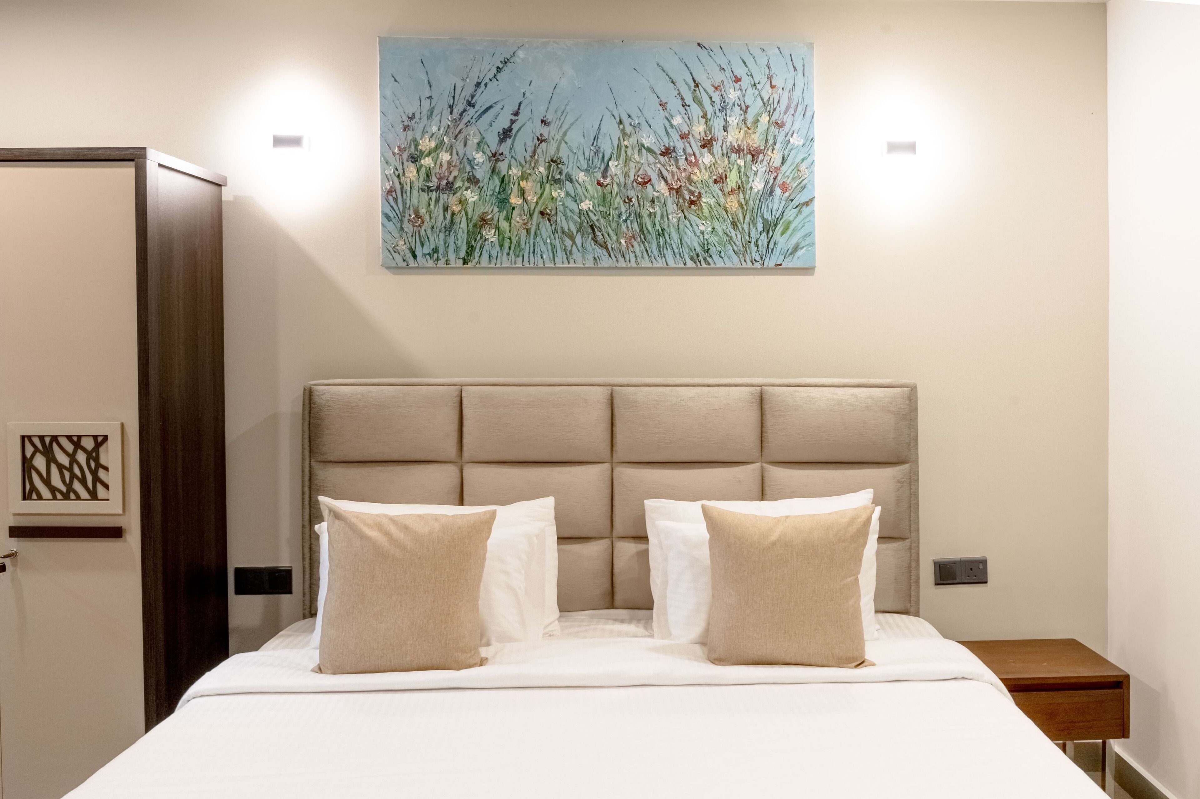 A hotel room with a large bed, a headboard, and a painting on the wall.
