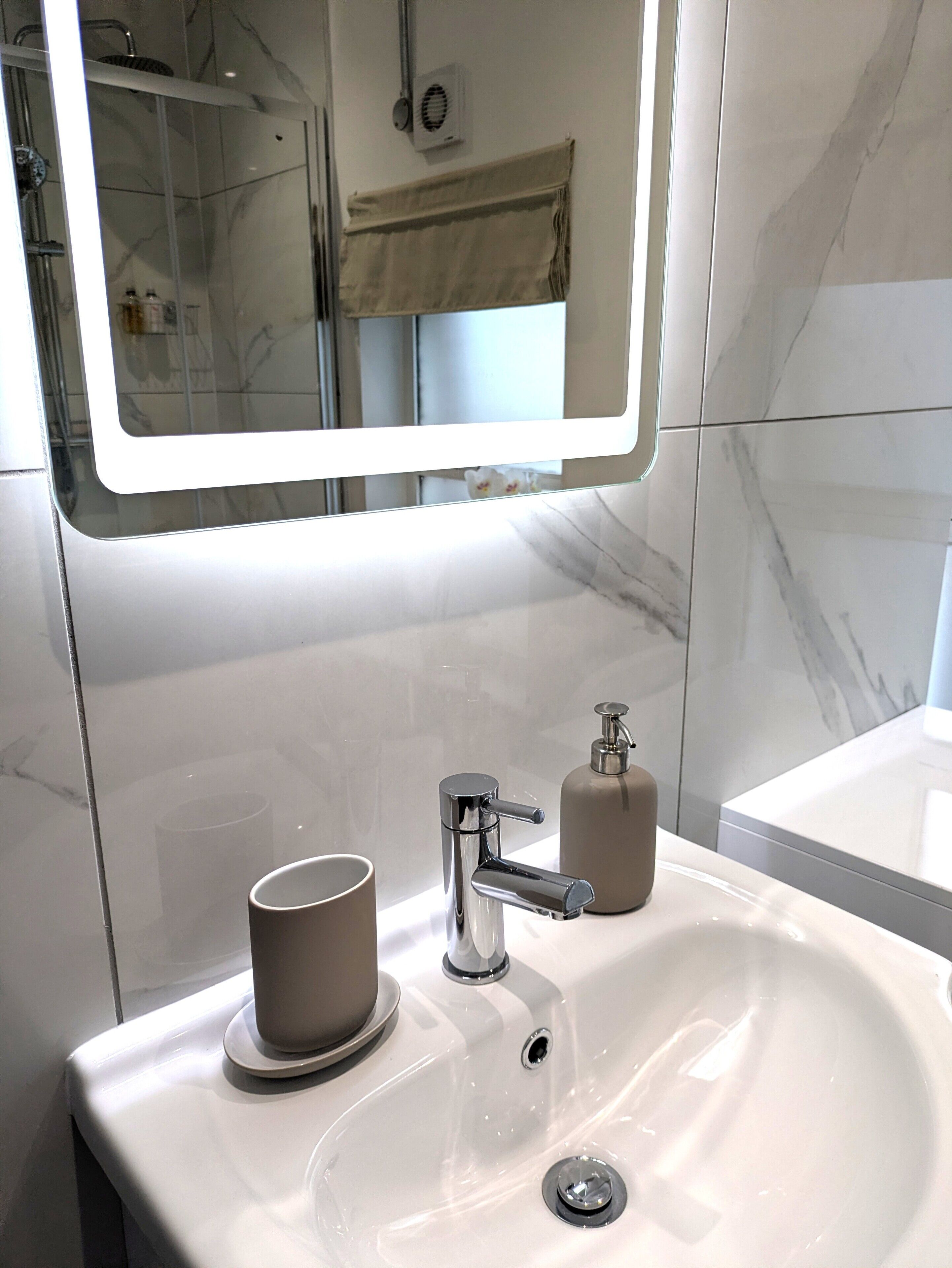 Un baño con un lavabo blanco, un espejo y una zona de ducha.