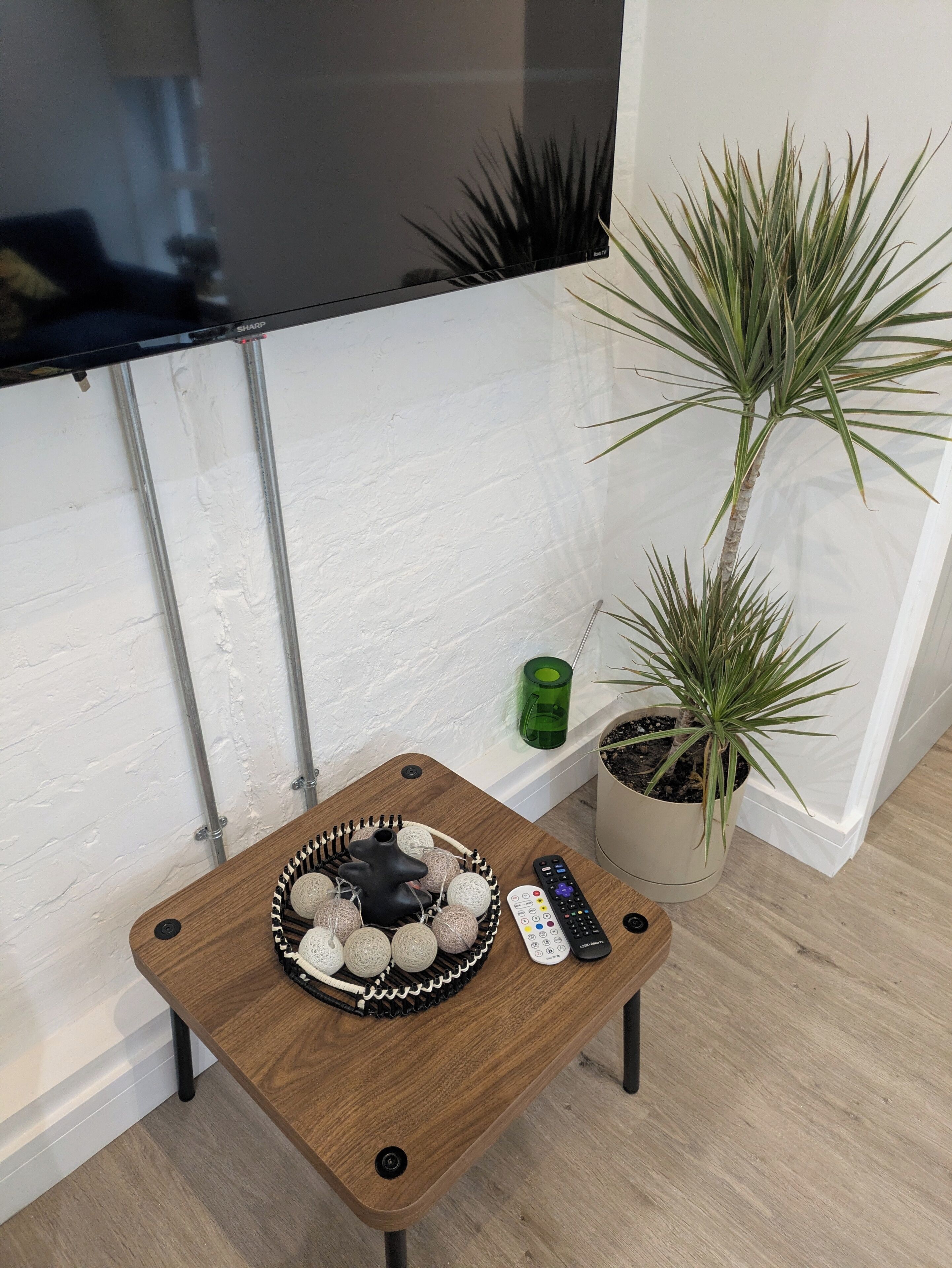 A small wooden table with a tray of decorative items, a remote control, and a potted plant.