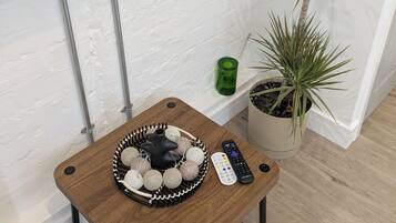 A small wooden table with a tray of decorative items, a remote control, and a potted plant.