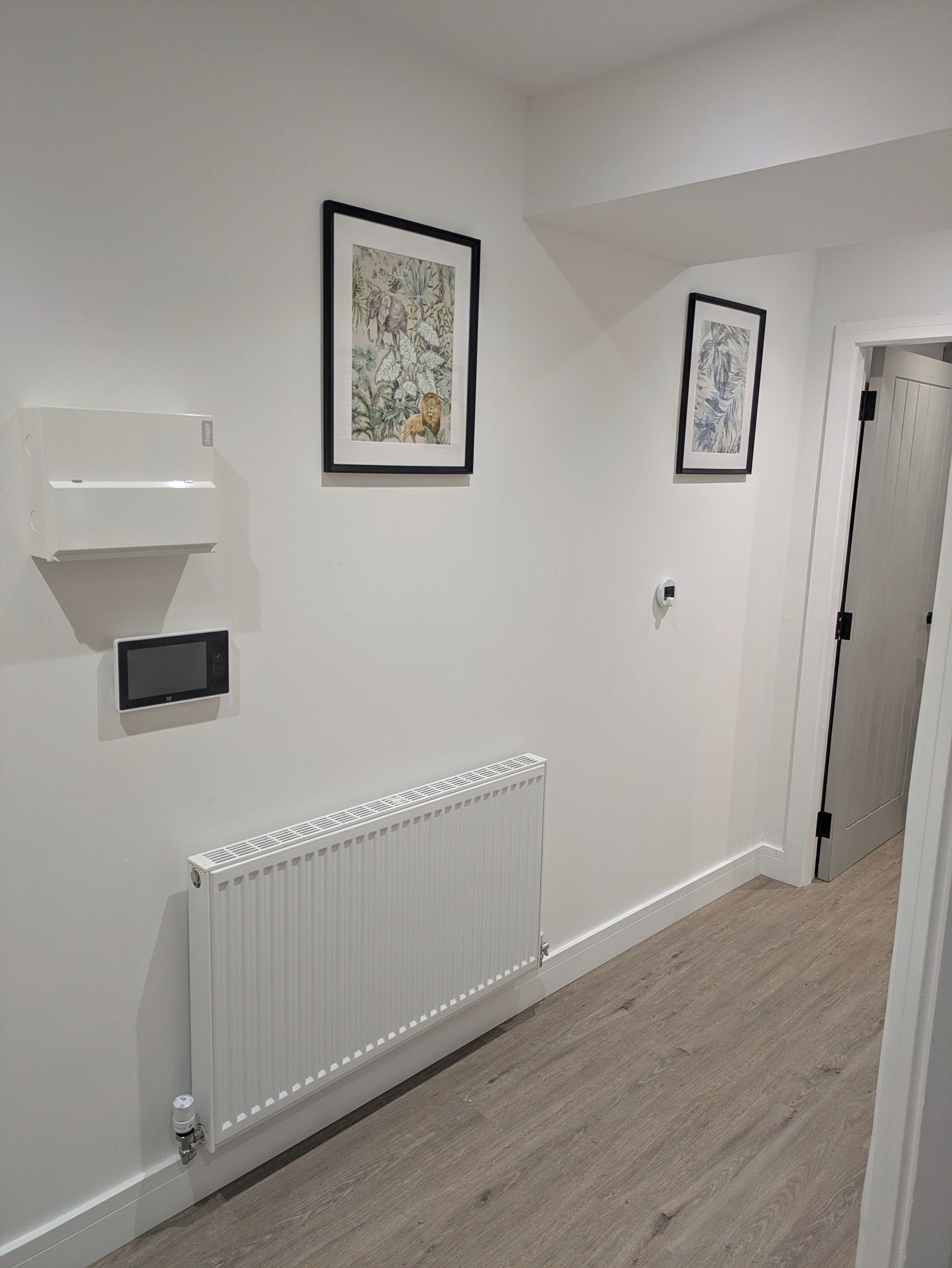 A hallway with white walls, a white radiator, and two framed artworks.