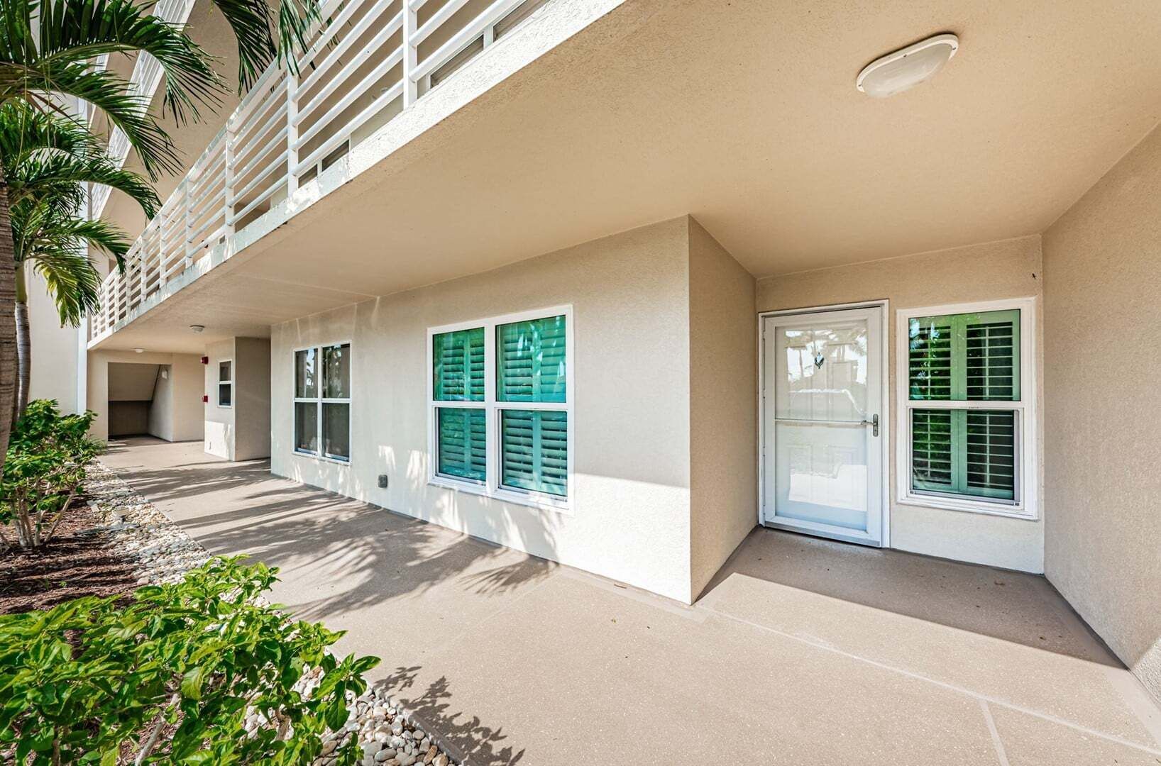 Un edificio con un corredor techado, varias ventanas con contraventanas y una puerta.