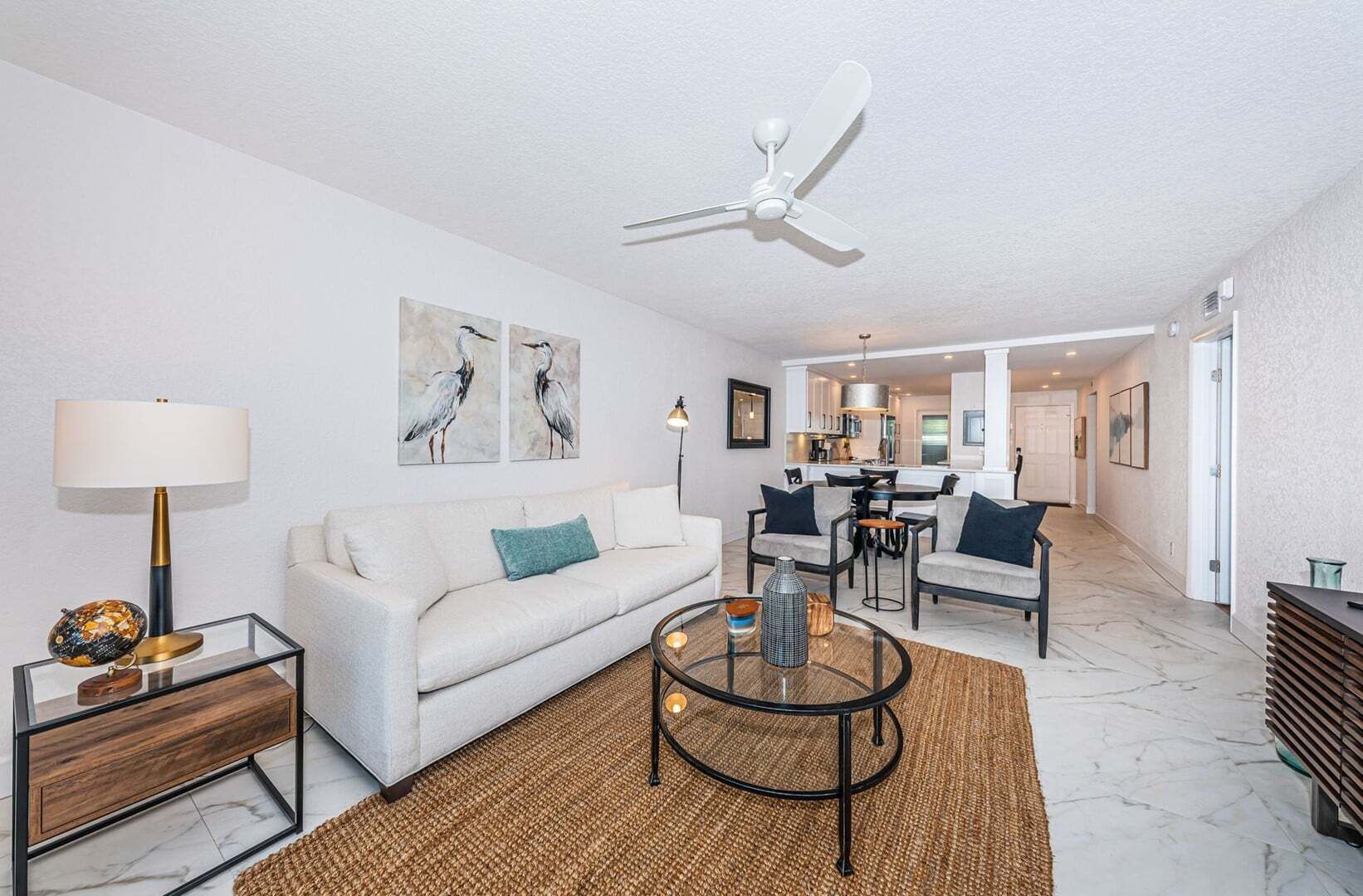 Un salon moderne avec un canapé blanc, une table basse en verre et un ventilateur de plafond.