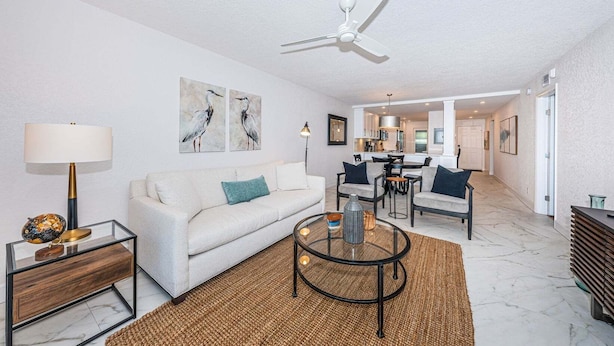 A modern living room with a white sofa, a glass coffee table, and a ceiling fan.