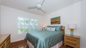 A bedroom with a bed, bedside lamps, a ceiling fan, a window with blinds, and a painting on the wall.
